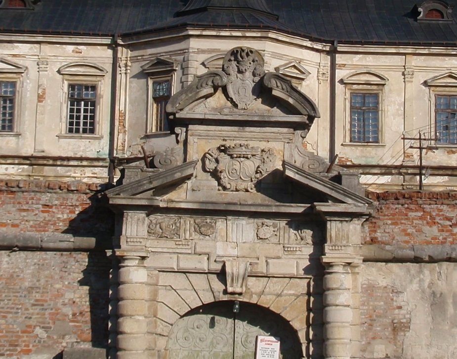 Вгорі над брамою замку видно герб "Кривда" роду Жевуських: голова лицаря у шоломі в короні з плюмажем, а під нею - підкова з хрестами
